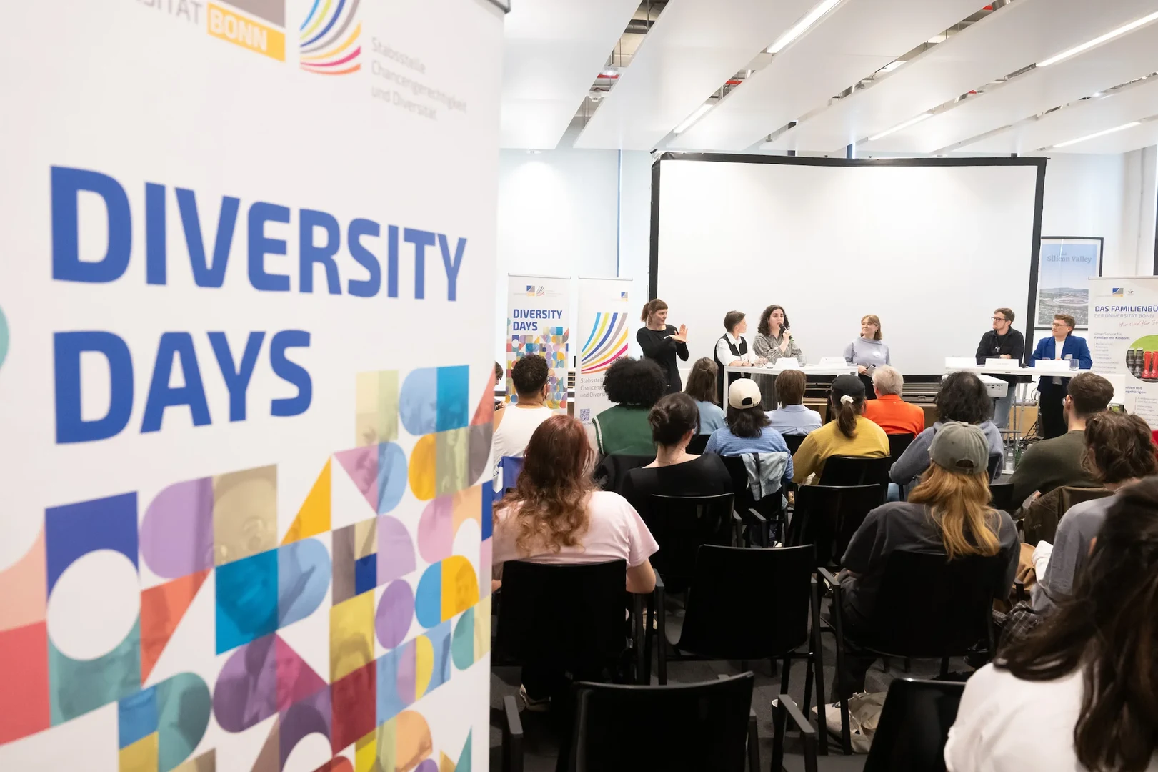 Foto einer Zuschauergruppe bei der Podiumsdiskussion, ein Roll-Up mit dem Diversity Days Logo im Vordergrund.
